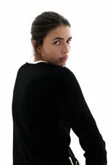 Saco negro de punto con ribetes blancos en cuello, bolsillos y borde inferior. Tiene corte entallado, cuello redondo, cierre frontal con botones dorados y solapas decorativas en el pecho y en la parte inferior.