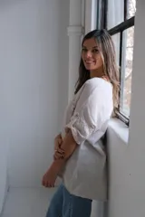 Blusa beige de lino con cuello redondo, mangas cortas con botón y bolsillo en el pecho con detalle de lentejuelas.