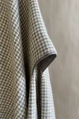 Poncho color beige con diseño a cuadros, cuello bote y terminaciones desflecadas. Tiene aberturas para los brazos en los laterales y detalles en cuero.