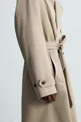 Trench largo regular fit color beige confeccionado en tejido italiano repelente al agua. Tiene cuello con solapas de pico, manga larga con puño ajustable con trabilla, bolsillos de vivo en cadera, bolsillo interior, cinturón del mismo tejido en cintura, bajo con abertura en centro espalda y cierre frontal de botonadura cruzada.
