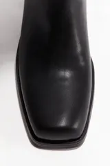Bota alta de cuero negro, estilo biker, con caña recta y punta cuadrada. Posee un taco de bloque bajo y forro interior de tejido.