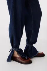 Pantalón de jean azul oscuro de corte recto, con cintura alta con cinturón del mismo material y detalle de flecos en la cintura y en los tobillos.