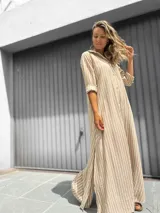 Vestido camisero largo con estampado de rayas verticales en beige y blanco. Presenta cuello camisero, cierre frontal con botones, mangas largas y tajos laterales en el ruedo.