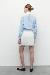 Minifalda de tweed blanca con detalle de flecos en la terminación, con un diseño elegante y sofisticado.