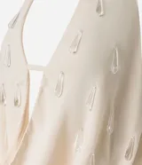 Blusa de crepé color crema, con escote drapeado y espalda descubierta. Presenta aplicaciones de piedras en el frente.