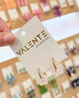 Aros tipo argolla de acero con dije colgante en forma de flor de acrílico color rosado.