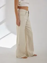 Pantalón gris de tiro medio alto, corte ancho, con bolsillos delanteros y traseros, detalles de atraques y triples costuras en color amarillo.