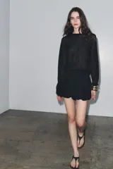 Falda pantalón corta negra de tiro medio, con cintura elastizada y detalle de tejido con volumen y pliegues. Cierre lateral con cremallera oculta.