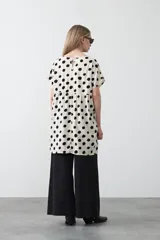 Vestido corto de silueta amplia con corte bajo busto, cuello a la base y mangas cortas. El tejido presenta un estampado de hojas en tonos rojo óxido y turquesa sobre un fondo de rayas verticales blancas y negras.