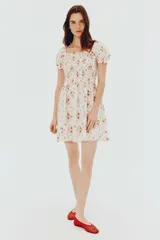 Vestido corto de popelina de algodón color blanco con estampado floral en tonos rosados. Tiene escote cuadrado con elástico, mangas cortas abullonadas con elástico y cuerpo fruncido.
