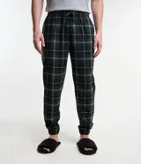 Pantalón de pijama masculino de fleece con estampado de cuadros en tonos verde, negro y blanco. Cuenta con cintura elástica, cordón de ajuste, bolsillos laterales y puños elásticos.