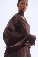 Vestido túnica largo color marrón oscuro, de tejido liviano, con cuello en V con lazos, mangas largas con puños abotonados y volados en mangas, laterales y ruedo.