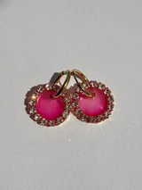 Aros colgantes con argolla dorada de acero quirúrgico y dije circular de resina fucsia con borde de strass.