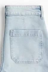 Pantalón de jean celeste de tiro alto, corte ancho, largo tobillero y bolsillos frontales con botón.