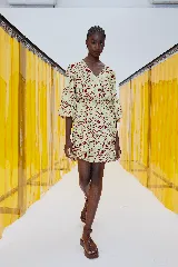 Vestido corto color amarillo con estampado abstracto en marrón, escote en V cruzado, mangas largas abullonadas con puños elásticos y falda con volantes.