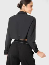 Blusa negra corta de manga larga con cuello camisero, cierre frontal con botones y dos bolsillos con fuelle en el pecho.