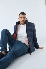 Campera inflada azul marino de nylon con cuello alto, cierre frontal con cremallera, bolsillos laterales con cierre y logo estampado en el pecho. El modelo usa talle M.