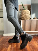 Borcego de cuero negro con puntera redondeada, cordones negros, paneles laterales de gamuza negra y detalle de cuero texturizado en el tobillo. Suela track de goma negra.