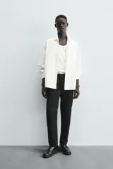 Pantalón chino negro de corte relajado (relaxed fit) con tiro medio, confeccionado en algodón con elasticidad. Presenta bolsillos delanteros y bolsillos traseros de vivo, con cierre frontal de cremallera y botón.