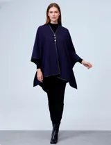 Ruana blanca de tejido suave, con ribete de eco cuero negro en los bordes y cierre frontal con botones metálicos dorados.