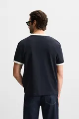 Camiseta azul marino de corte recto, con cuello redondo y mangas cortas. Presenta ribete blanco en cuello y mangas.