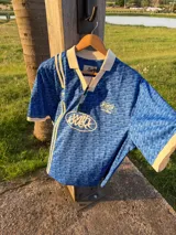 Polo de manga corta con cuello tipo polo y escote en V, corte boxy fit. Presenta un patrón texturizado en relieve y un logo ovalado con la inscripción "with love" en el pecho.