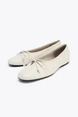 Zapato tipo bailarina color crema, de piel efecto soft, con detalle de lazo en la parte delantera y acabado en punta redonda.