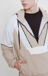 Anorak unisex beige y blanco con capucha, cierre parcial con cremallera, bolsillo tipo canguro con solapa y cordones ajustables con texto en la capucha.