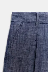 Bermuda azul con textura de lino, tiro alto, cintura con trabillas, bolsillos laterales ocultos en costura, detalle de pliegues en delantero y cierre frontal con cremallera, botón y ganchos metálicos.