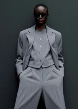 Blazer gris con estampado de raya diplomática, cuello con solapa, cierre de botones en la parte delantera, manga larga con puños abotonados, hombreras y dos bolsillos de solapa en la parte delantera.