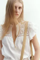Blusa blanca de algodón con corte holgado, cuello mao y mangas cortas con volados. Presenta broderie en el canesú delantero.