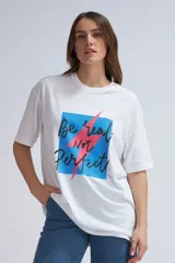 Camiseta blanca de corte holgado con estampado frontal que incluye un cuadrado azul con bordes negros y la frase "Be real Not Perfect" en letras negras con un rayo rosa que atraviesa el estampado.