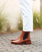 Botas estilo Chelsea de cuero vacuno color marrón con textura grabada tipo reptil. Presentan paneles elásticos laterales en color negro, puntera almendrada y taco cuadrado de madera.