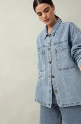 Sobrecamisa oversize de jean azul con cuello camisero, cierre frontal con botones, mangas largas y bolsillos de parche en el pecho.