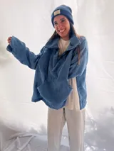 Buzo de pana fina color verde oliva, con diseño de corte holgado y mangas largas. Presenta una textura de cordón vertical característica de la pana y un pequeño parche decorativo en la parte superior de la espalda.