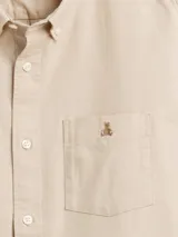 Camisa de manga larga color beige, de corte clásico, con cuello abotonado, bolsillo en el pecho y logo de oso bordado.