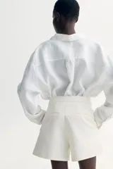 Short de vestir color blanco, de tiro alto, con bolsillos al bies y bolsillos insertados decorativos atrás. Presenta cierre frontal con botón.