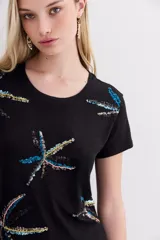 Remera de mangas cortas color crudo, de calce relajado y escote redondo. El frente se encuentra bordado con un diseño de palmeras en lentejuelas y canutillos.