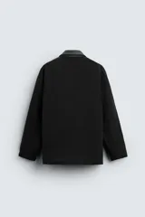 Parka negra de algodón con cuello solapa de cuero sintético, corte recto, acolchada, con bolsillos de parche y cierre frontal con botones.