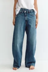 Jeans de tiro medio color azul denim, corte baggy, con trabillas y cinco bolsillos. Cierre frontal asimétrico con cremallera y botones metálicos.