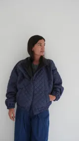 Campera puffer azul marino con diseño acolchado de rombos, cuello de cuero sintético negro, mangas largas abullonadas con puños elásticos y cierre frontal con cremallera.