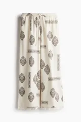 Pantalón de corte holgado en tejido liviano de mezcla de lino y viscosa, color crudo con estampado paisley en marrón. Modelo con cintura elástica fruncida y cordón para ajustar, bolsillos laterales discretos y piernas rectas con bajo deshilachado.