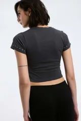 Remera blanca de algodón con cuello redondo y mangas cortas, con detalle de tachas plateadas en cuello y mangas.