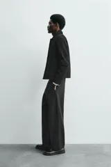 Cazadora de corte cropped fit, confeccionada en piel con acabado serraje (gamuza) de color negro. Presenta cuello solapa, manga larga, dos bolsillos de plastrón en la cadera y cierre frontal de botonadura.