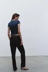 Pantalón negro de tiro alto con pernera recta, bolsillos frontales y falsos bolsillos con solapa en la espalda. Incluye cinturón marrón de cuero sintético.