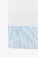Camiseta blanca de cuello redondo con solapa combinada a contraste de rayas celestes. Manga corta. Bajo con tejido combinado de rayas celestes. Cierre en espalda con abertura y botón.