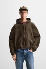 Cazadora relaxed fit confeccionada en tejido de algodón denim color marrón. Cuello con capucha ajustable y manga larga. Bolsillos frontales tipo canguro. Acabados con elástico. Efecto lavado. Cierre frontal de cremallera.