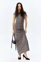 Vestido largo gris de punto elástico con leve brillo, corte entallado, escote drapeado, espalda escotada y pliegues laterales para crear un efecto drapeado. Sin mangas.