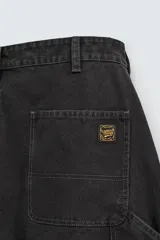 Pantalón negro de corte amplio, confeccionado en tejido de algodón con efecto lavado. Presenta bolsillos frontales, traseros de parche, tira multifunción y bolsillos laterales en las perneras. Cuenta con cierre frontal con cremallera y botón.