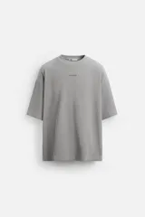 Camiseta gris de corte relaxed fit, cuello redondo y manga corta. Tiene un parche rectangular con texto en el pecho.